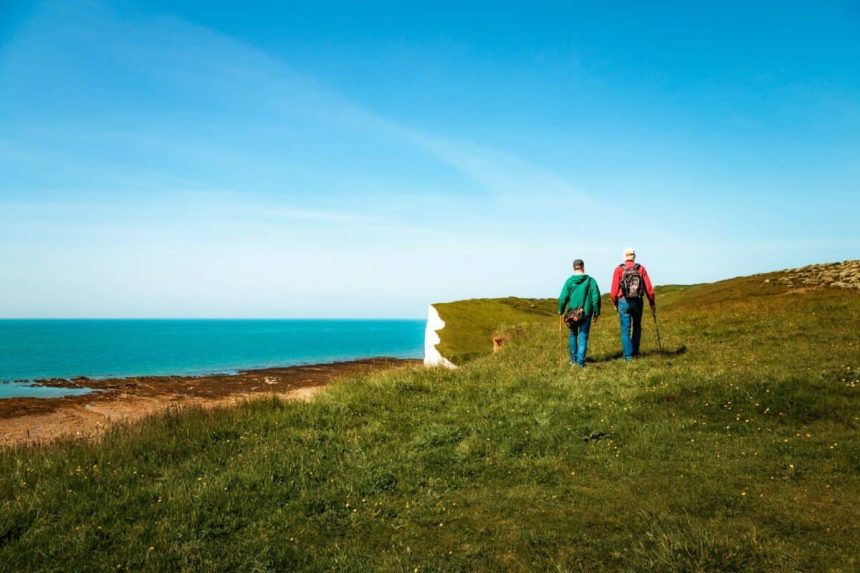 Rear view image depicting two men hiking together with the stunning backdrop of Seven Sisters cliffs in the south of England.