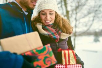 Smiling diverse couple holding Christmas presents while walking through a winter forest