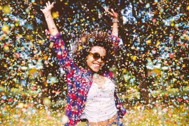 Young mixed-race woman jumping for joy in a park with confetti falling around her