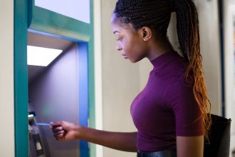 Young Black woman using a debit card at an ATM to withdraw money