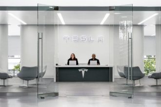 Two employees sat at desk welcoming customer to a Tesla car showroom