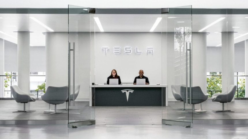 Two employees sat at desk welcoming customer to a Tesla car showroom