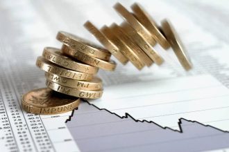 Stack of British pound coins falling on list of share prices