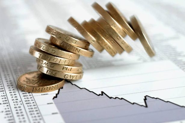 Stack of British pound coins falling on list of share prices