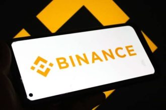 Logo de Binance atrás con el logo de Binance en un teléfono inteligente