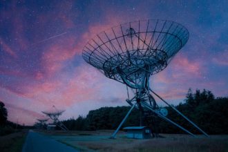 A row of satellite radars at night