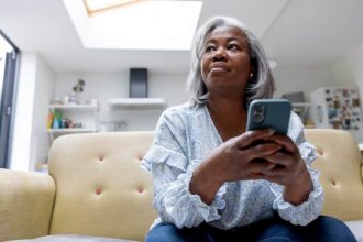 Mature black woman at home texting on her cell phone while sitting on the couch